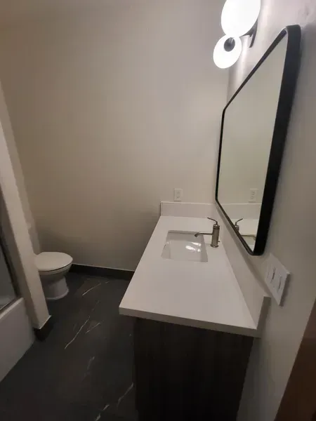 Bathroom with a white countertop, large mirror, and toilet. Dark floor and gray walls.