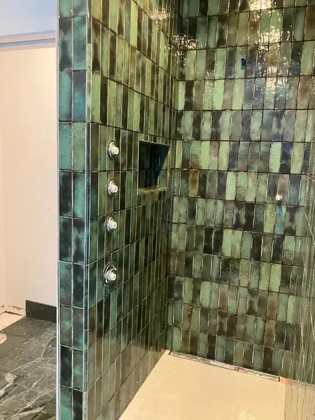 Green and black tiled shower with inset shelf and silver shower fixtures.
