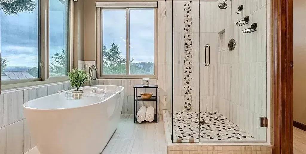 Bathroom with white soaking tub, glass shower, window. Tile and wood accents.