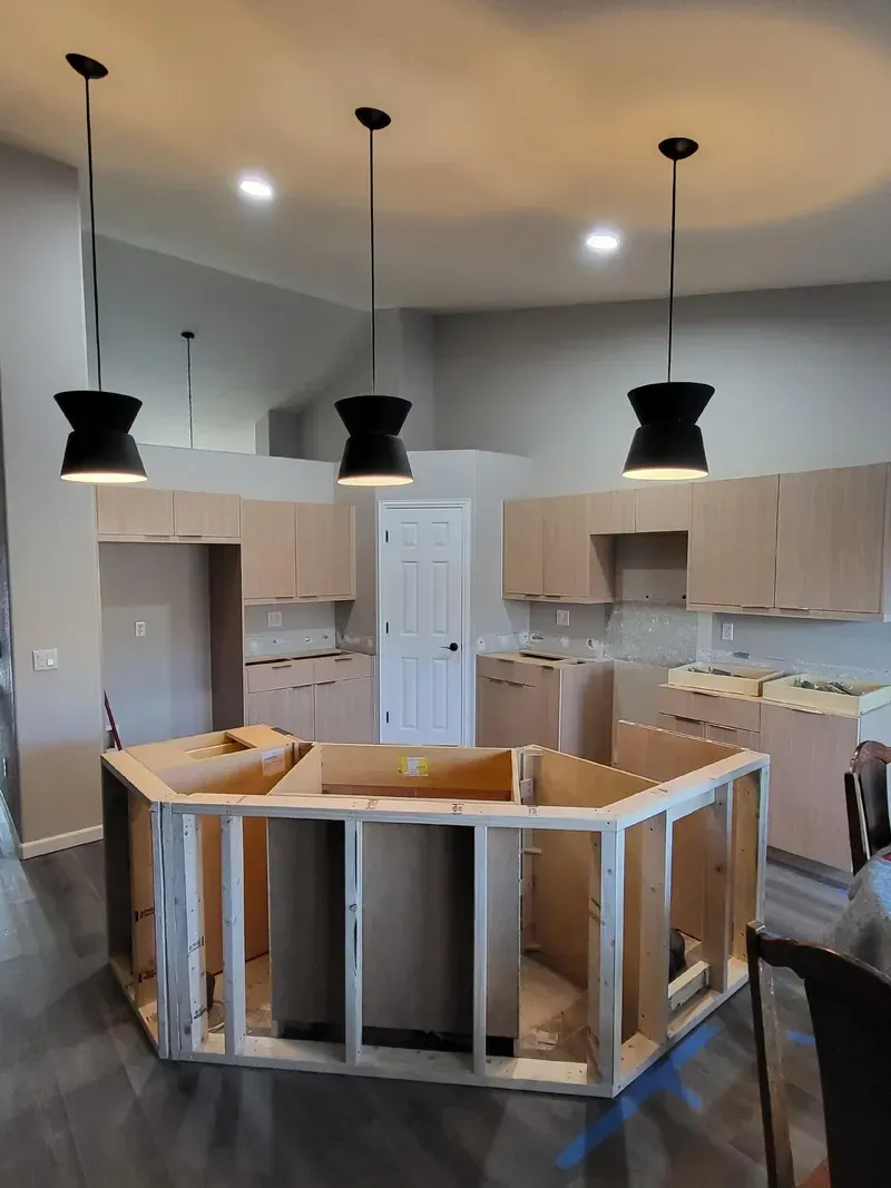 Kitchen renovation: unfinished island frame with three black pendant lights and light-colored cabinets.
