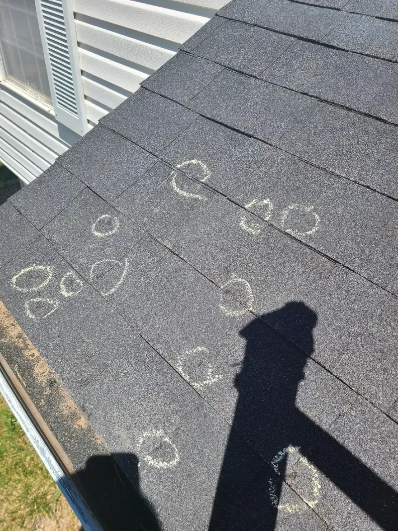 Dark asphalt shingle roof with multiple circular indentations, possibly hail damage, viewed from above.