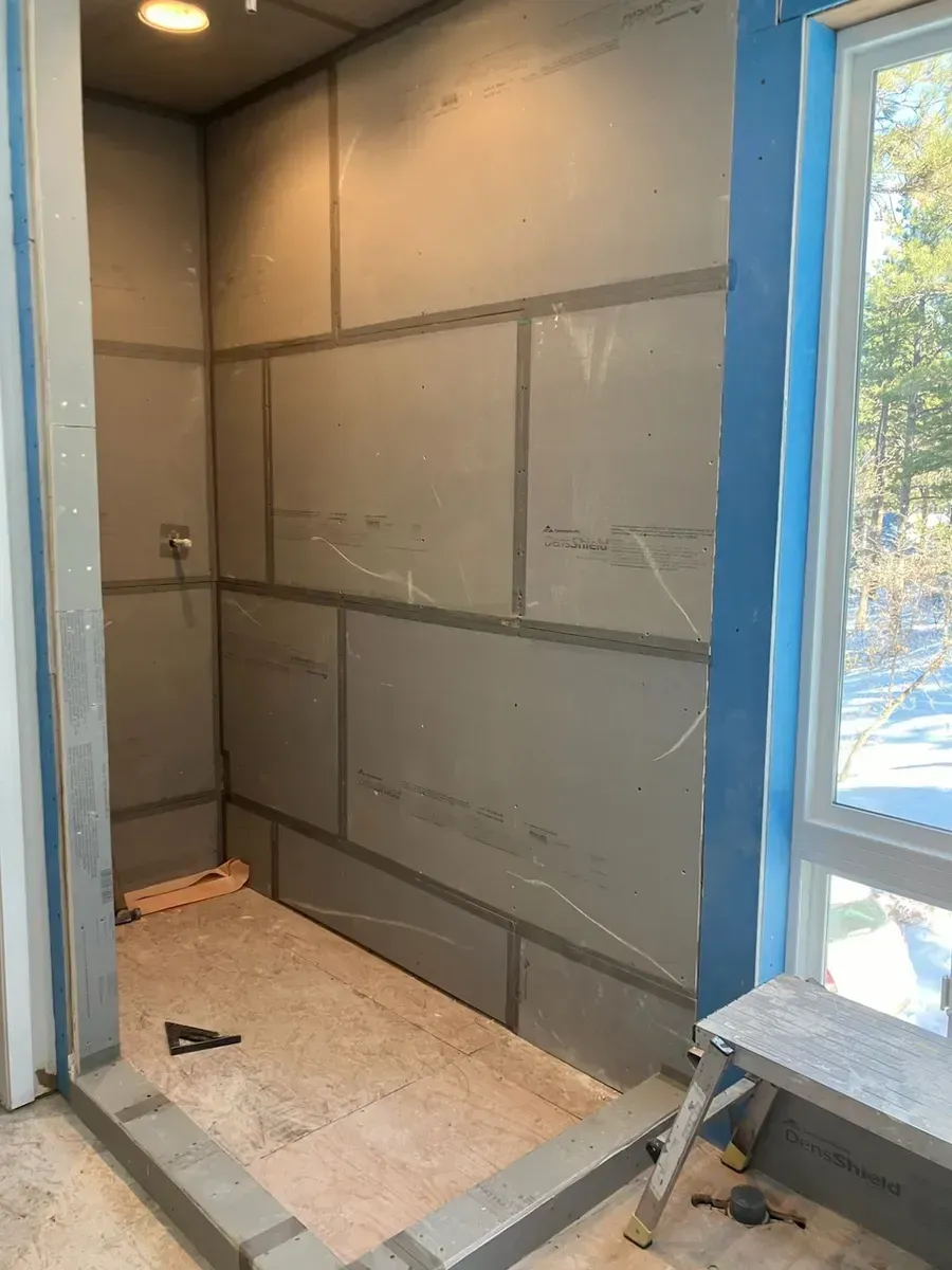 Shower stall with gray walls and flooring under construction, next to a window.