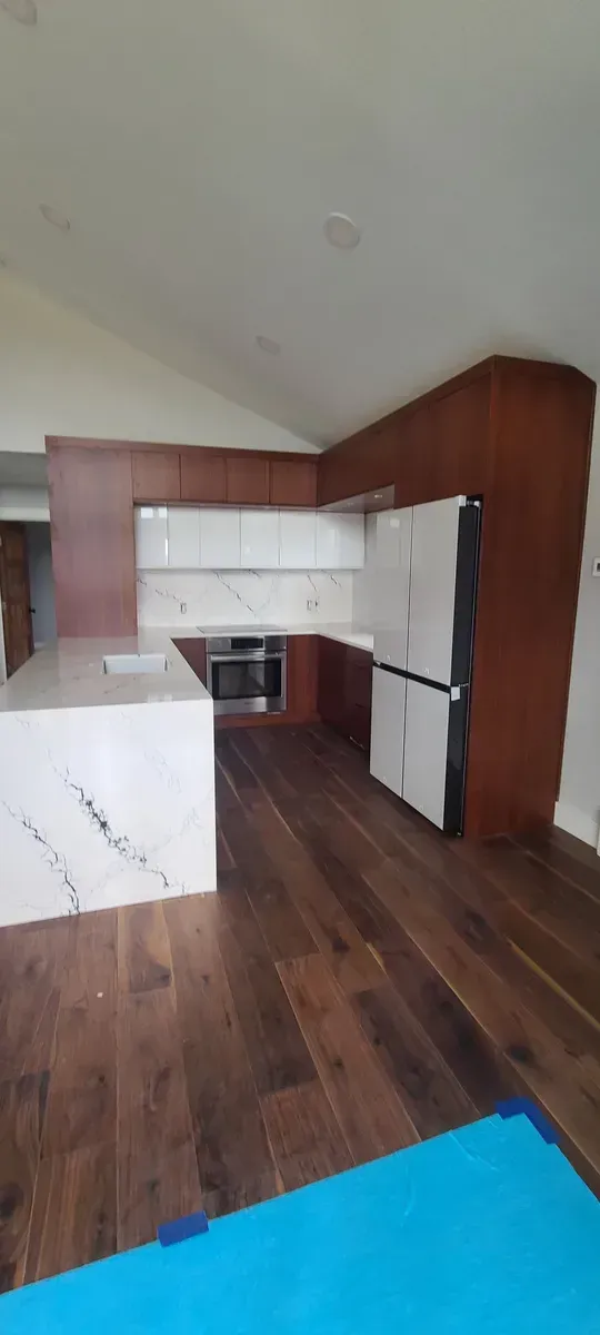 Modern kitchen with dark wood cabinets, white countertops with gray veining, and hardwood floors.