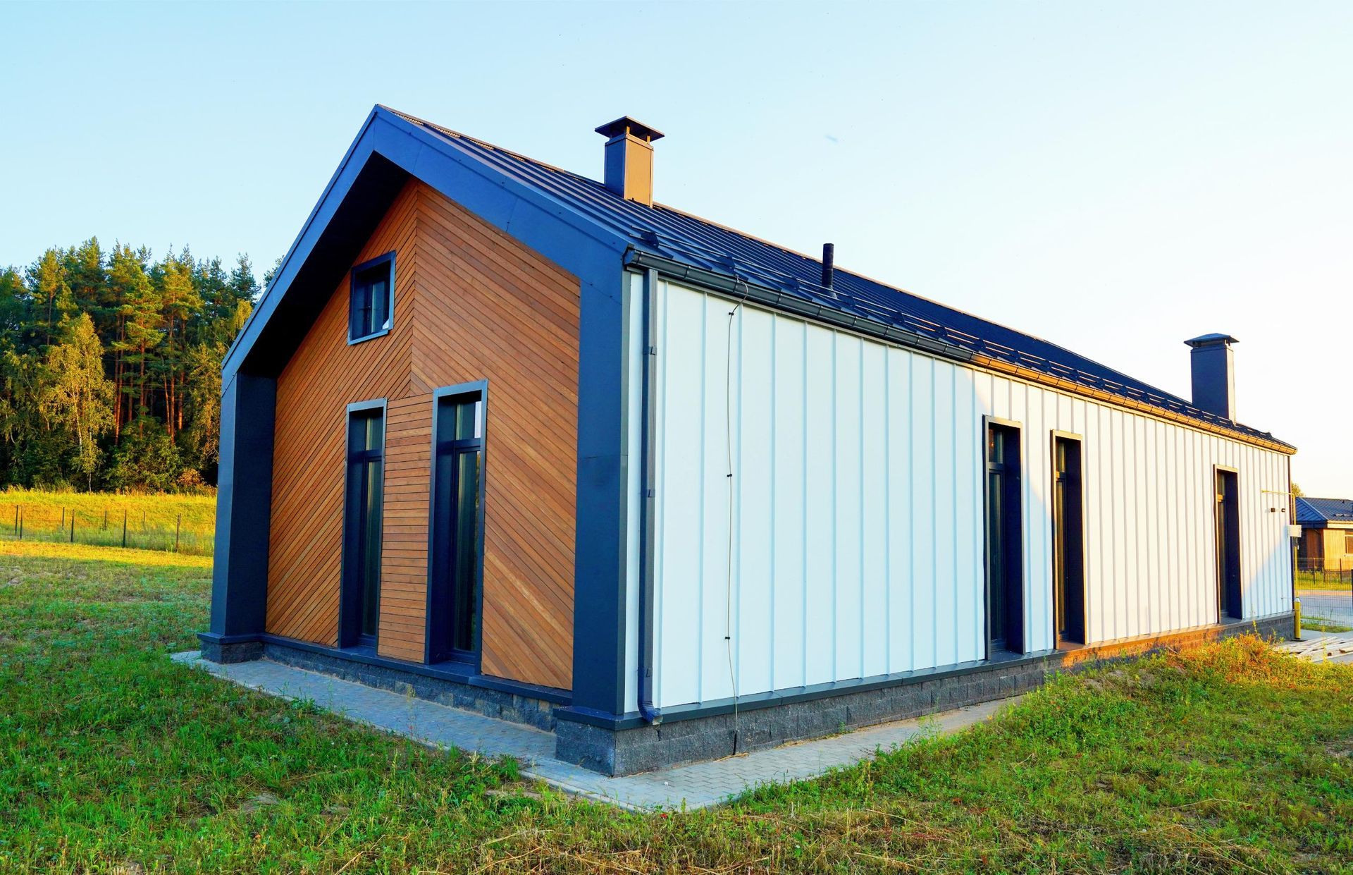 A modern, rectangular cabin with a gabled roof, featuring wood-slatted siding on one end and white vertical metal walls.