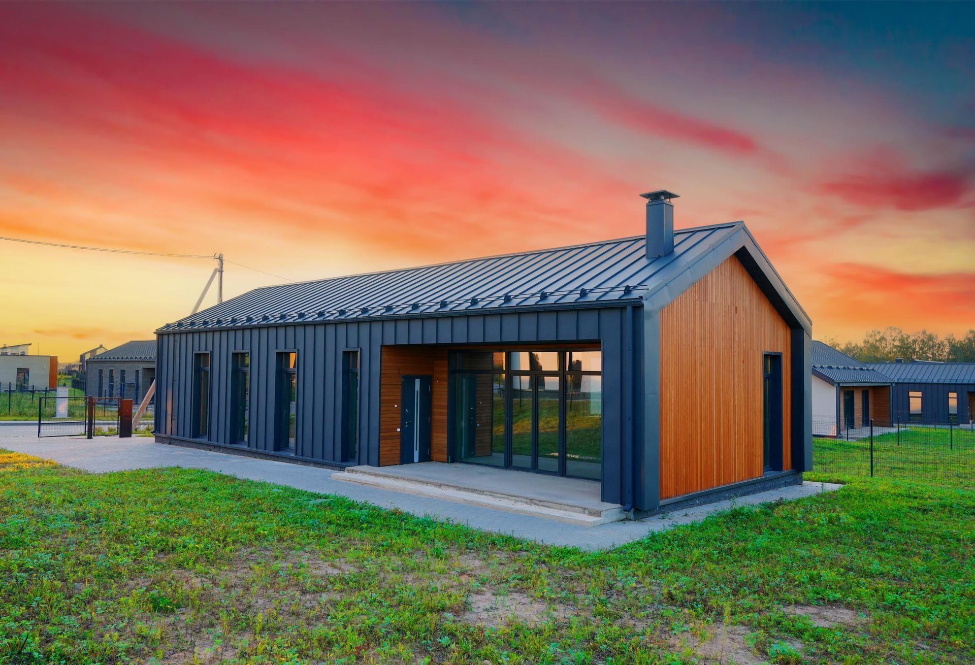 A modern, rectangular house with black metal siding and wood accents, set against a vibrant sunset sky.
