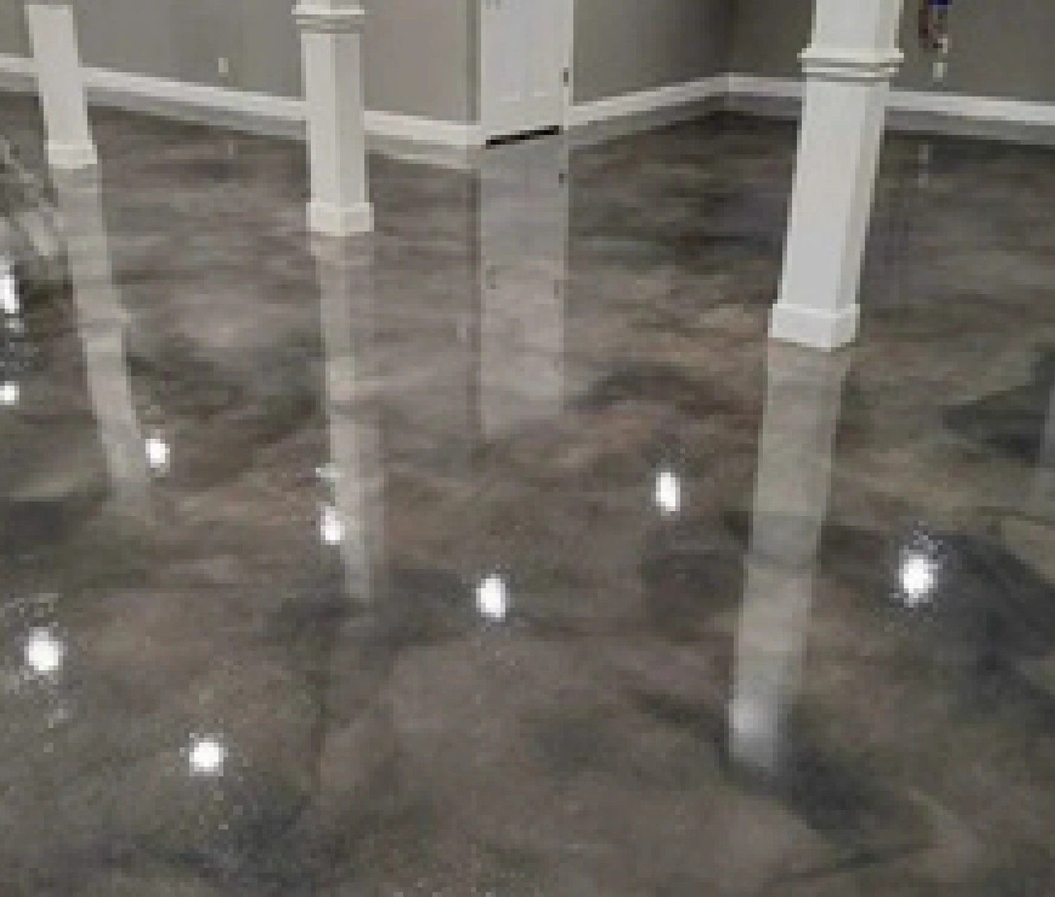 A basement with a shiny metallic floor and white pillars.