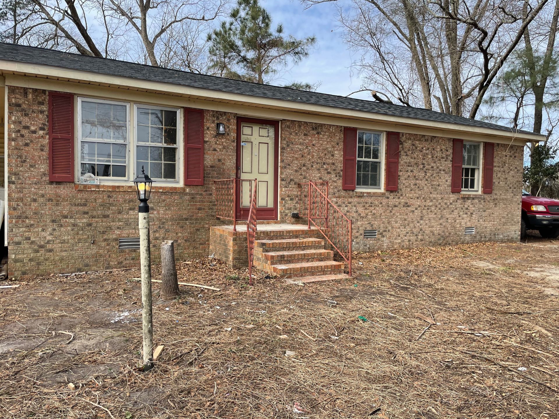 A brick house with red shutters and a car parked in front of it.