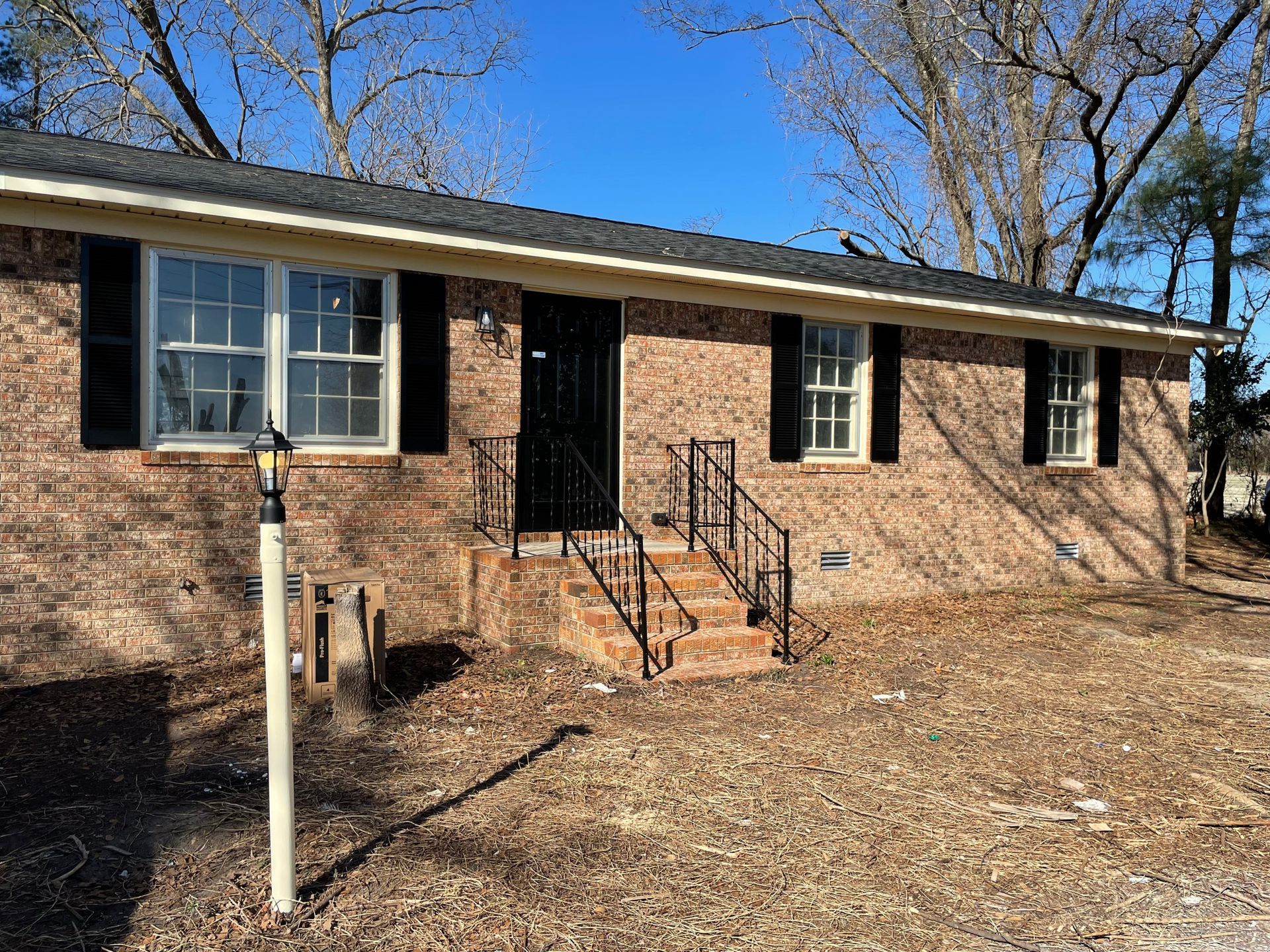 A brick house with black shutters and stairs is for sale.