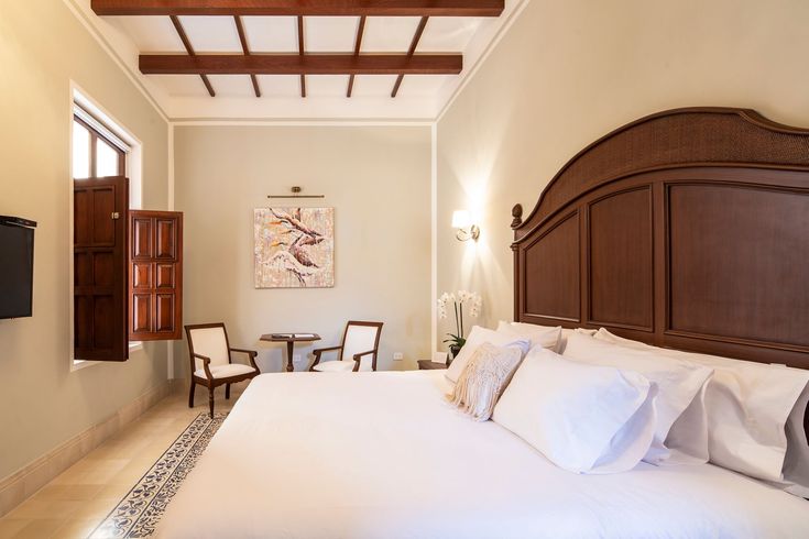 Dormitorio con cama king size, sillas y obras de arte. Cuenta con vigas de madera en el techo, ventana con persianas.