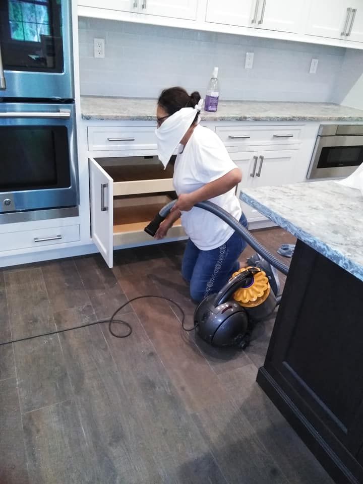A woman wearing a mask is using a vacuum cleaner in a kitchen.