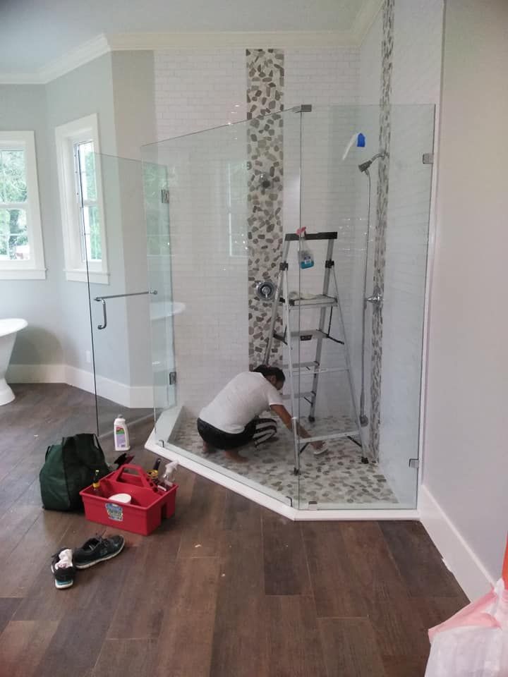 A man is working on a glass shower door in a bathroom.