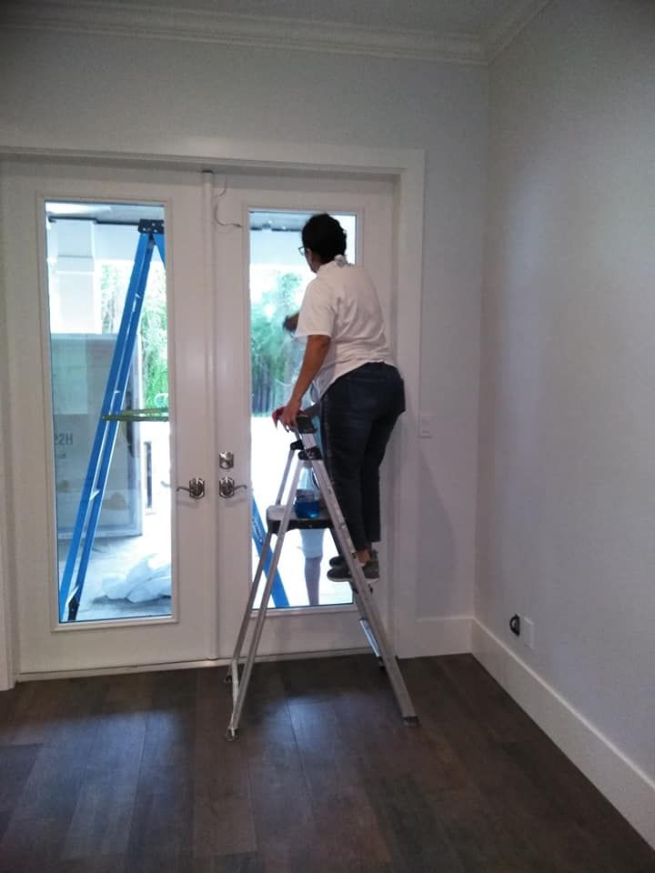A woman is standing on a ladder cleaning a door