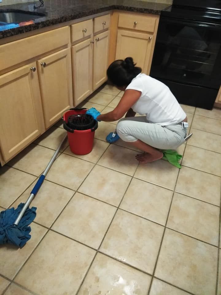 A woman is kneeling down in a kitchen with a mop and bucket