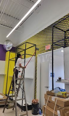 A woman is standing on a ladder painting a wall in a store.