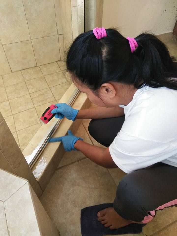 A woman is cleaning a shower door with a sponge.