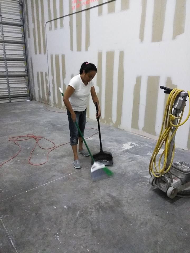 A woman is sweeping the floor in a warehouse with a broom.
