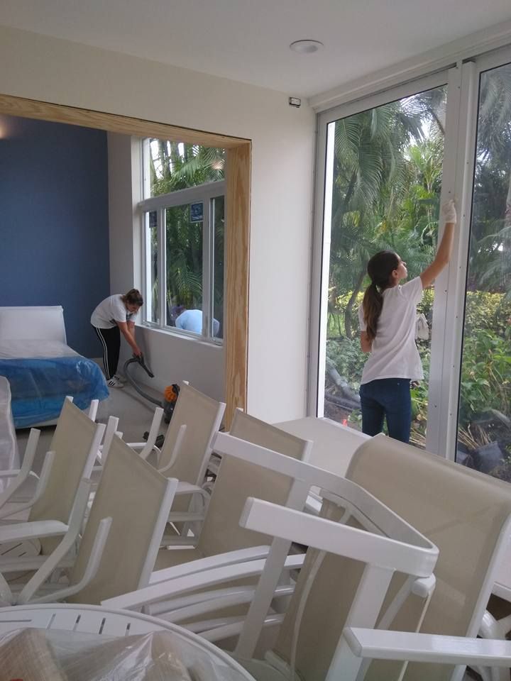 A woman is cleaning a window in a room with chairs.