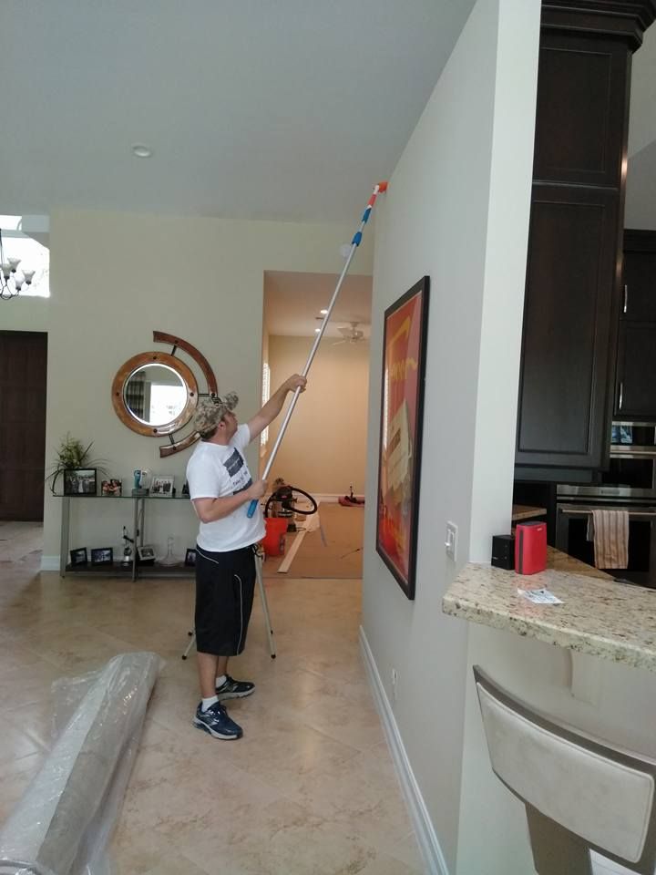 A man is painting a wall with a long pole in a living room.