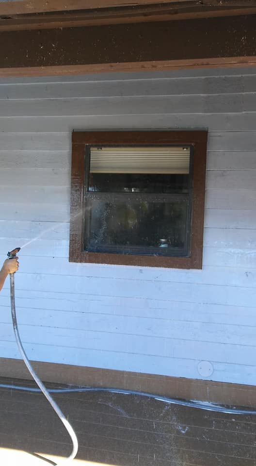 A person is spraying water on a white house with a window.
