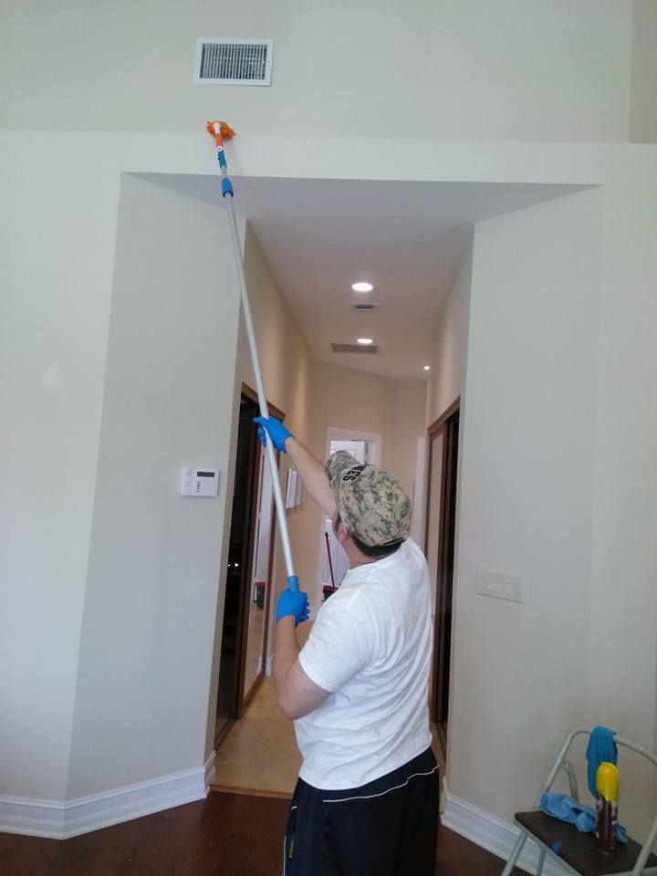 A man is cleaning the ceiling of a house with a mop.