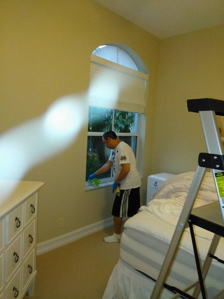 A man is cleaning a window in a bedroom next to a ladder