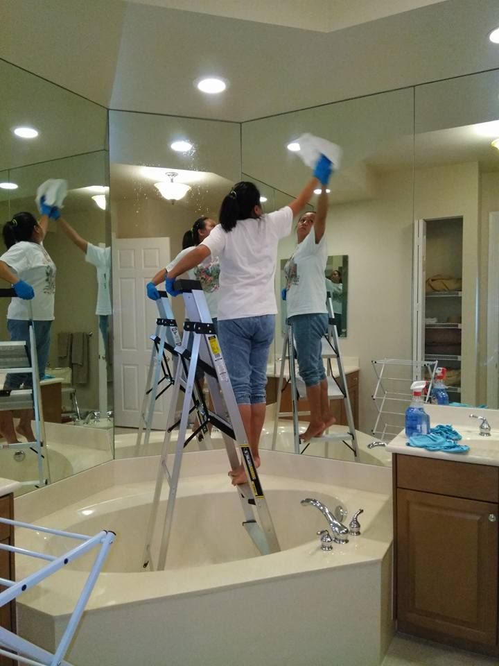 Two women are cleaning a mirror in a bathroom