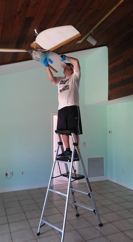 A man is standing on a ladder fixing a ceiling fan