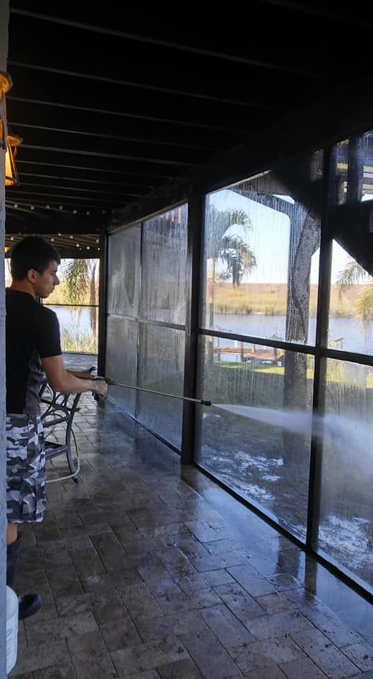 A man is cleaning a screened in porch with a high pressure washer.