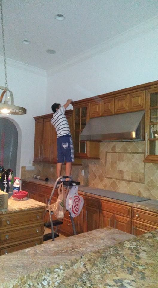 A man is standing on a ladder in a kitchen cleaning cabinets.