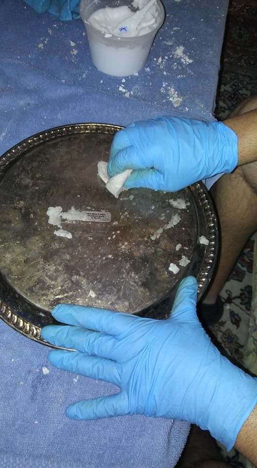 A person wearing blue gloves is cleaning a silver tray.
