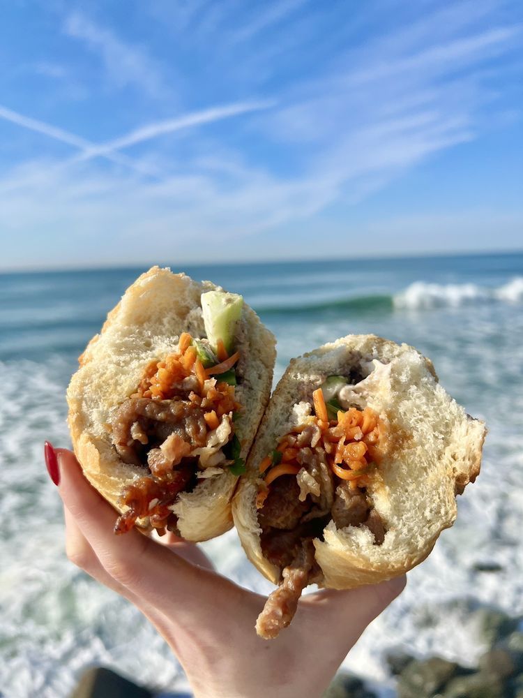 A person is holding a sandwich in front of the ocean.