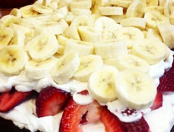 A cake with bananas and strawberries on top of whipped cream