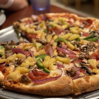 A pizza with pineapple , mushrooms , onions and peppers on a pan