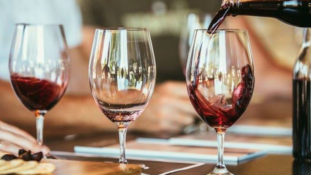 A person is pouring red wine into three glasses on a table.