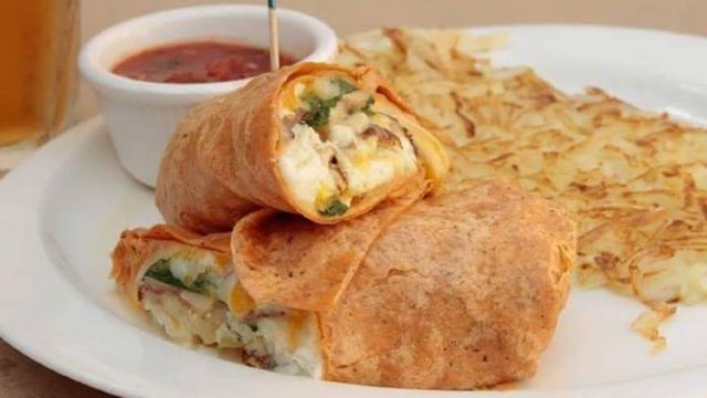 A white plate topped with a wrap and hash browns.