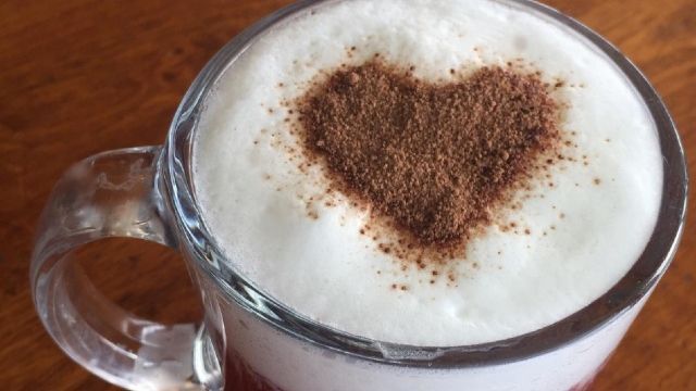 A cup of cappuccino with a heart shaped foam on top.