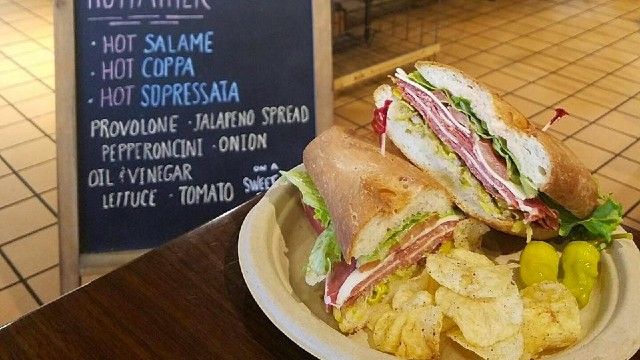 A sandwich and chips are on a plate in front of a chalkboard.