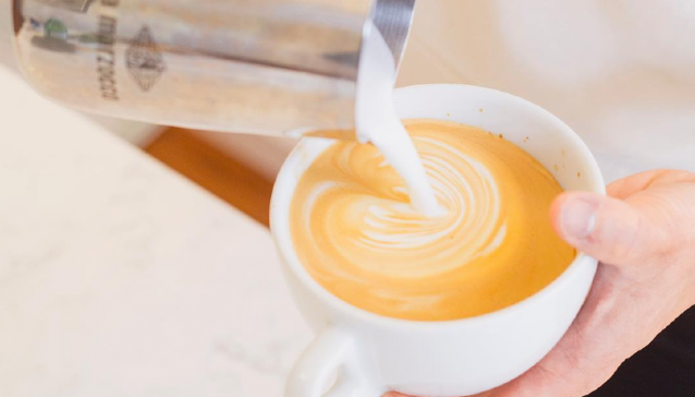A person is pouring milk into a cup of coffee.