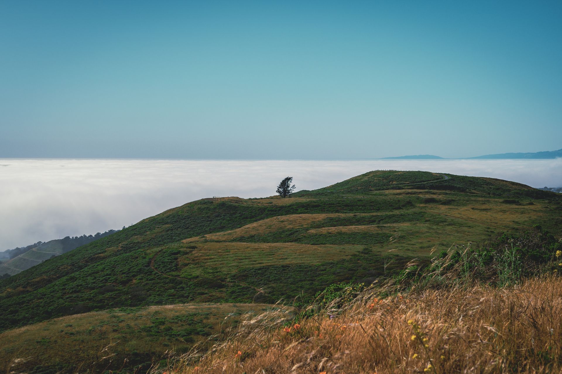 A person is sitting on top of a hill overlooking a cloudy sky.