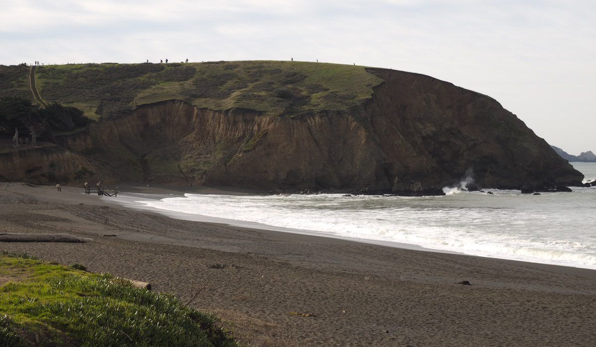 A beach with a cliff in the background and waves crashing on the shore.