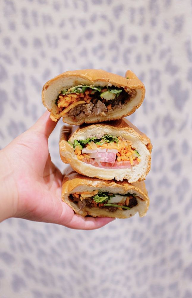 A person is holding three sandwiches stacked on top of each other.
