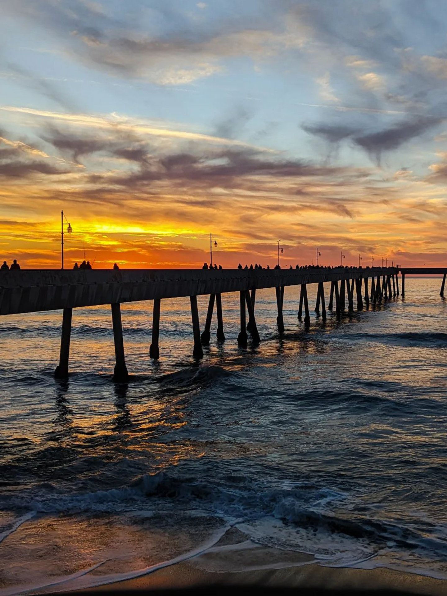 A pier overlooking the ocean at sunset with people walking on it.