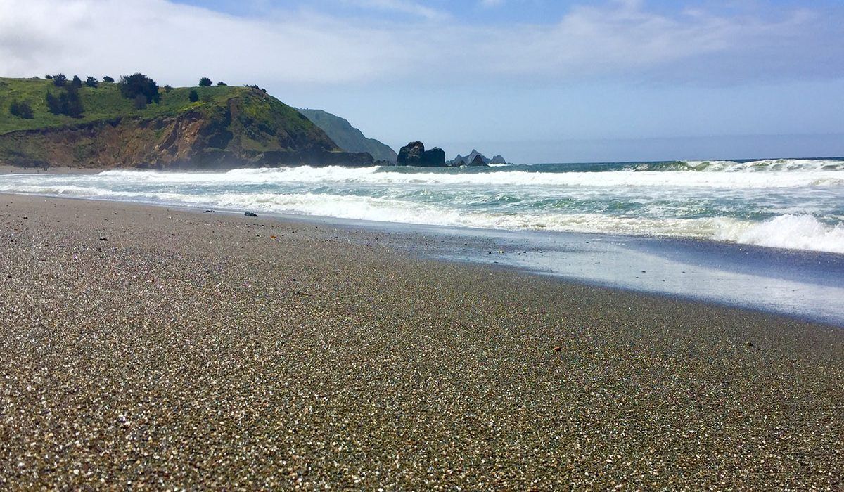 A beach with waves crashing on the shore and a hill in the background.