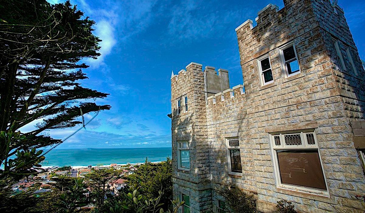 A castle with a view of the ocean is surrounded by trees.