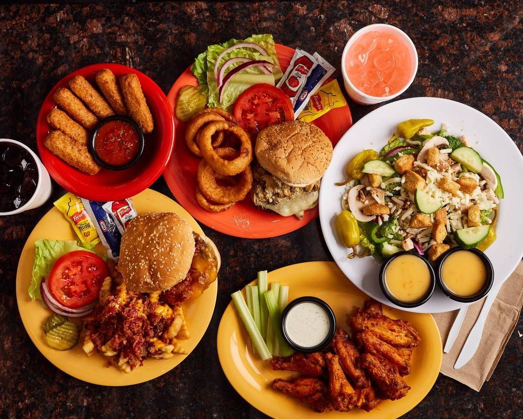 A table topped with plates of food including hamburgers onion rings and chicken wings
