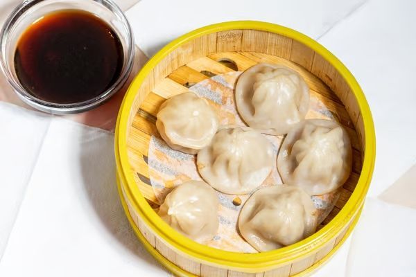 A bamboo steamer filled with dumplings next to a bowl of dipping sauce.