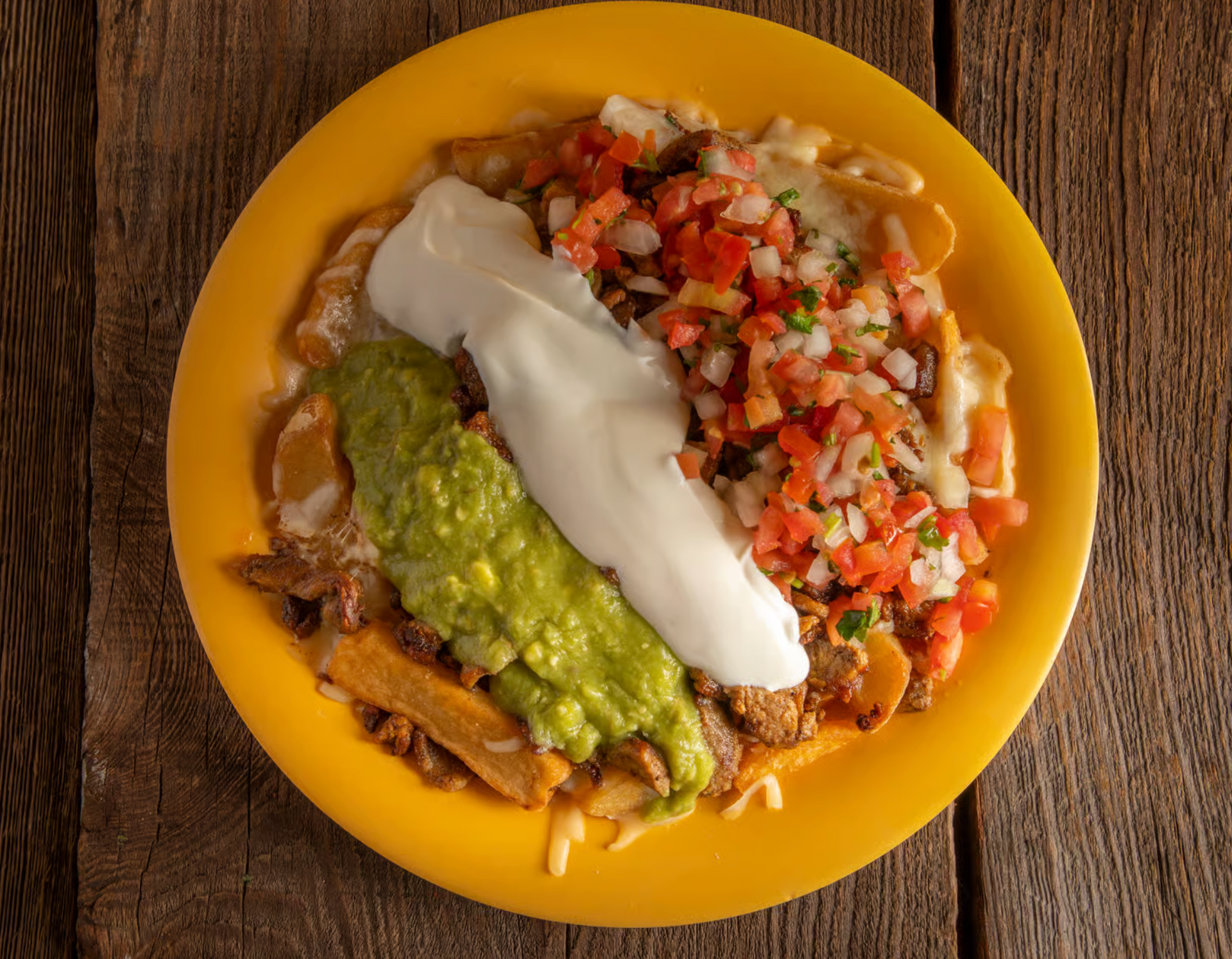 A yellow plate topped with guacamole and sour cream on a wooden table.