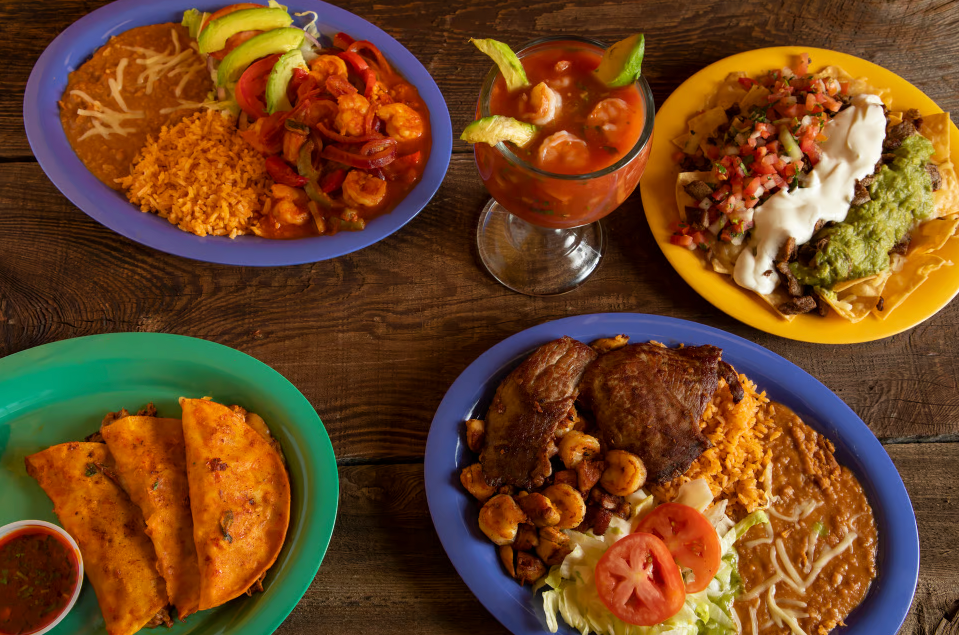 Four plates of mexican food are on a wooden table.