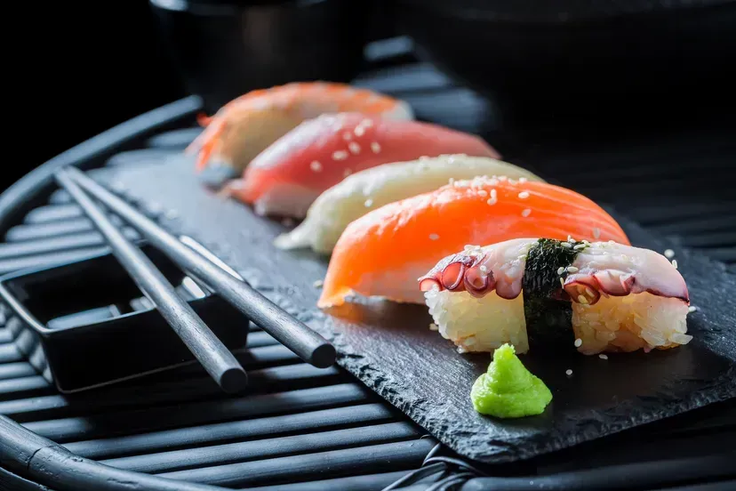 A tray of sushi with chopsticks and wasabi on a table.