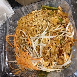 A plastic container filled with noodles , vegetables and nuts.